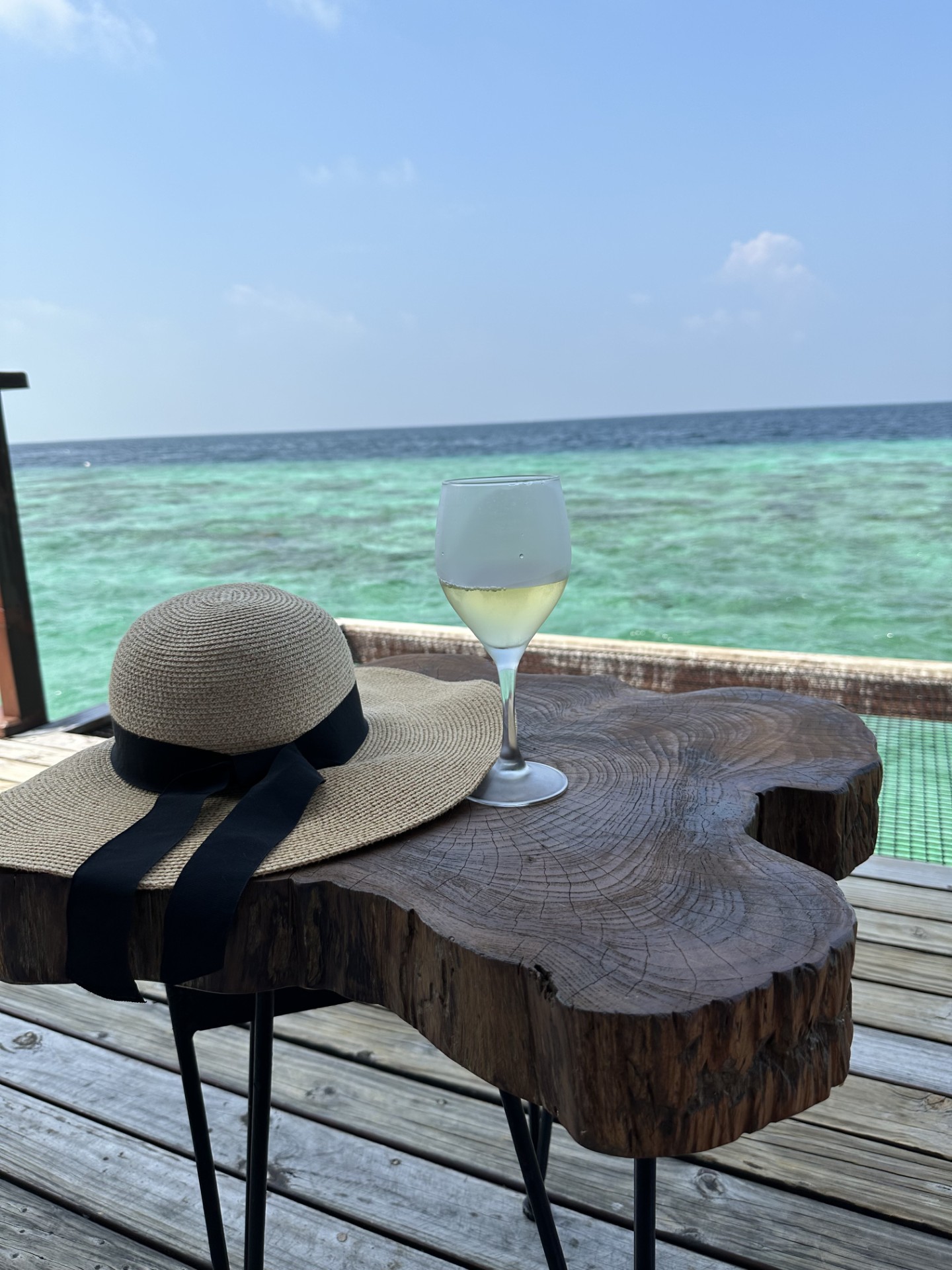 Sunhat with wine glass on table overlooking blue water