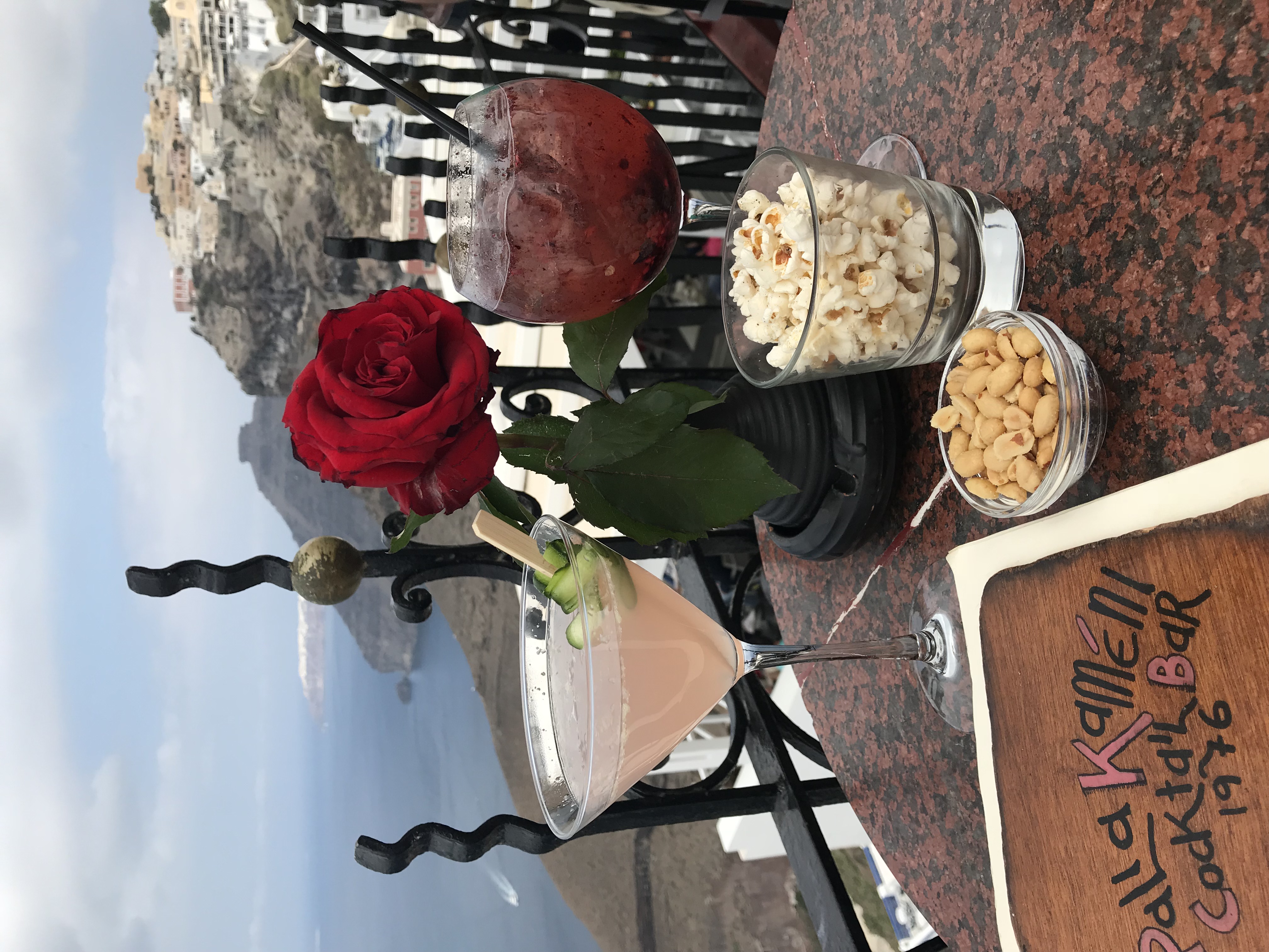 Drinks, snacks, flower on table overlooking Greece coastline